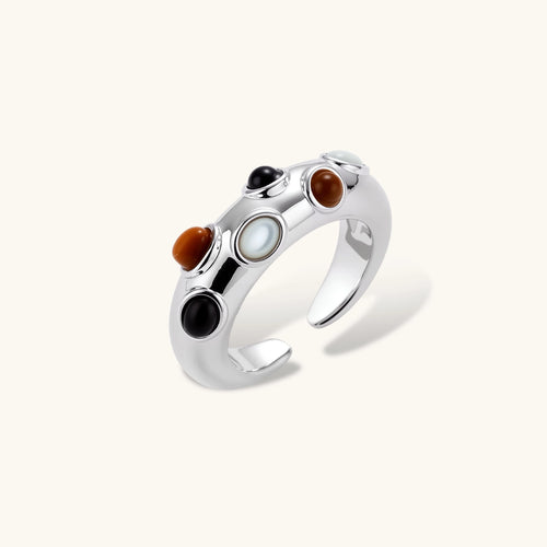 Chunky silver-tone adjustable open ring with black, brown and milky white oval cabochon stones on a cream background.