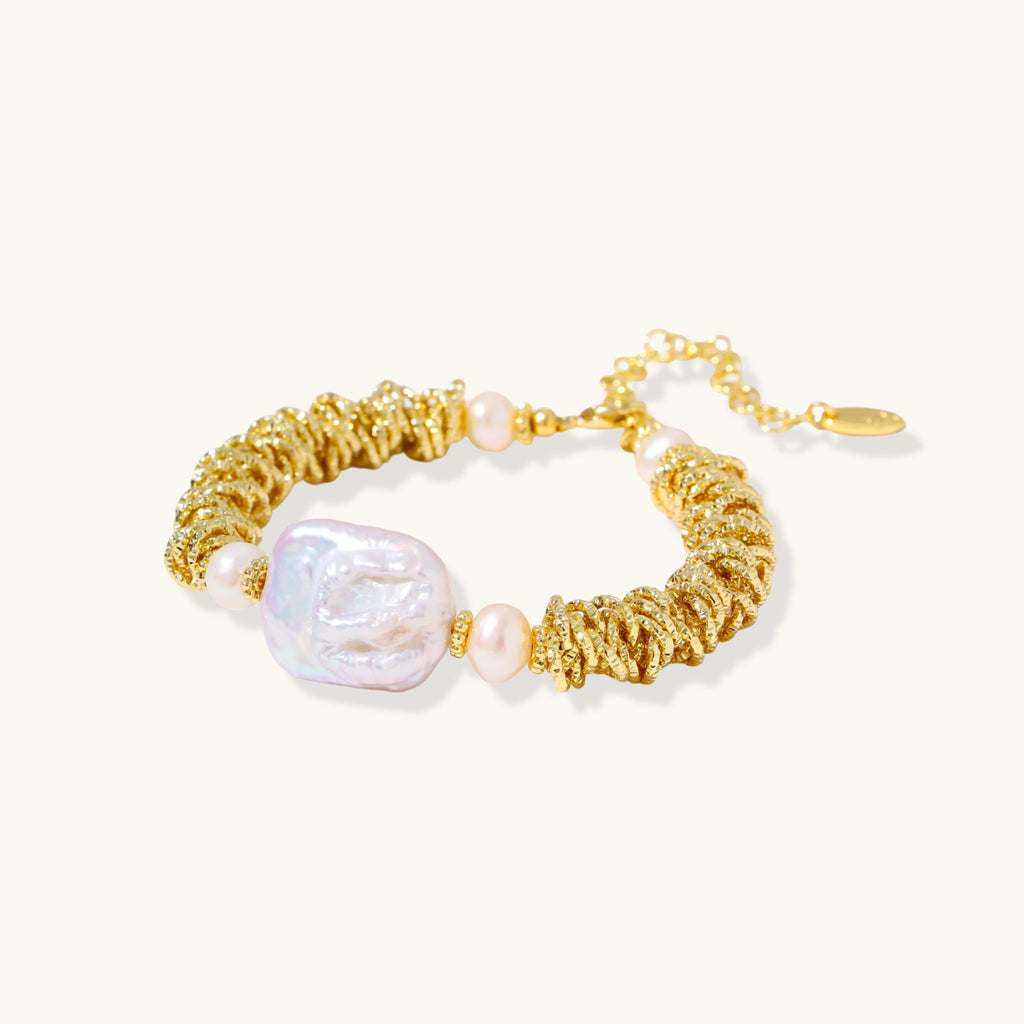 18k gold-plated bracelet with textured wave segments, baroque pearl centerpiece, and round freshwater pearls on cream background