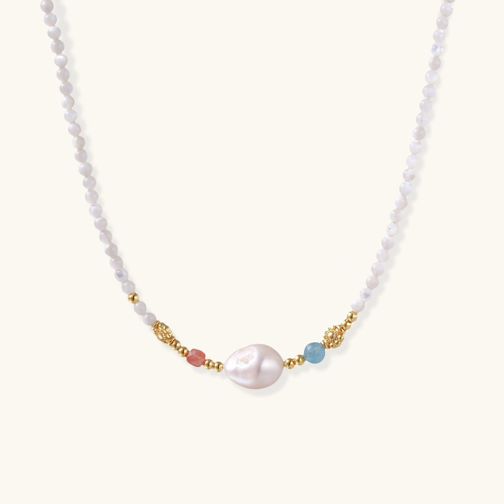 Dainty white beaded necklace with a central freshwater pearl, peach and blue beads and gold vermeil accents on a cream background.
