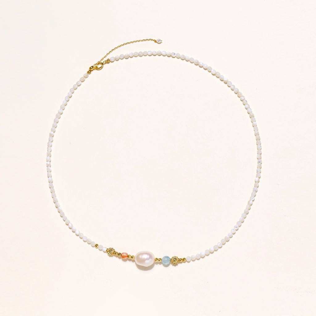 Dainty white beaded necklace with a central freshwater pearl, peach and blue beads and gold vermeil accents on a cream background.