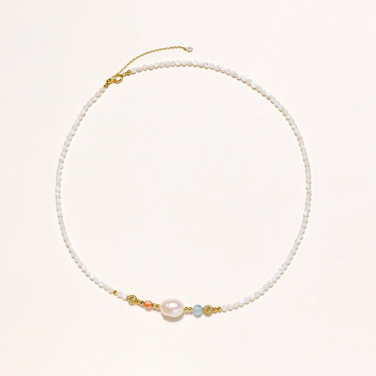 Dainty white beaded necklace with a central freshwater pearl, peach and blue beads and gold vermeil accents on a cream background.