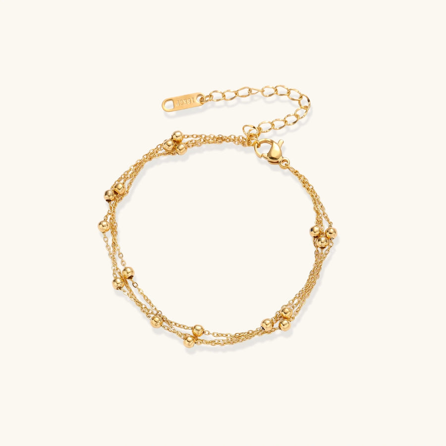 Three-strand gold-plated bracelet with clustered ball beads and adjustable clasp on cream background