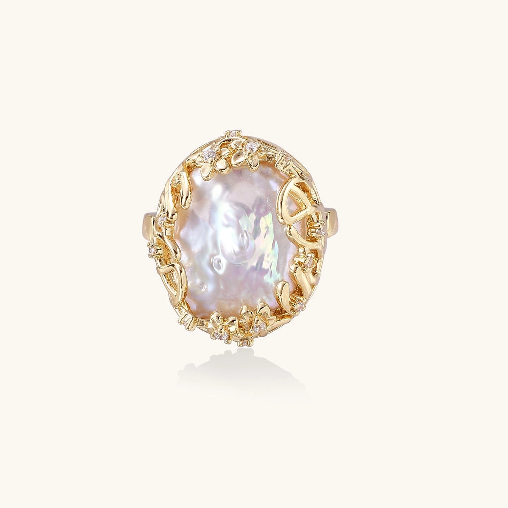Gold filigree crown ring cradling an iridescent baroque freshwater pearl with crystal accents on white background