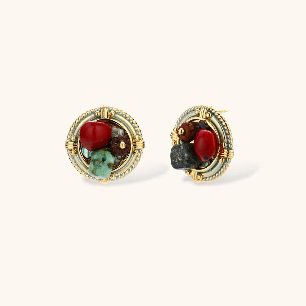 Pair of round gold-plated stud earrings with rope-twist borders, a red bead, brown wood bead and green turquoise on cream.
