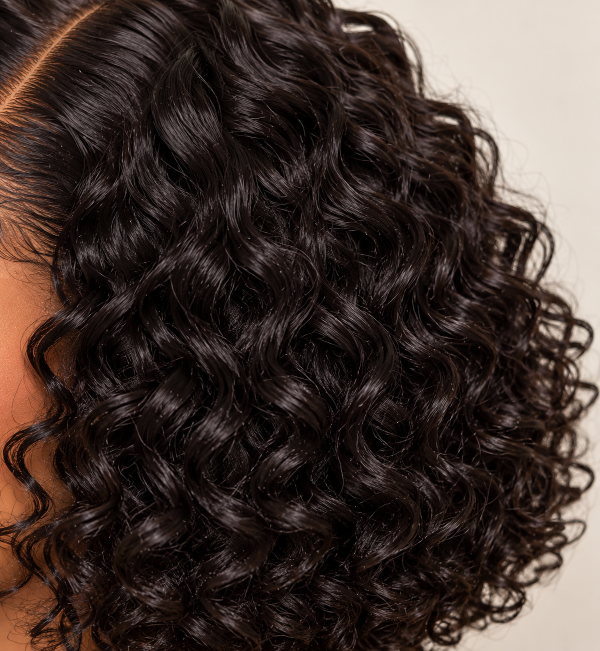 Close-up of a person's head showing the back of a long, dark brown to near-black curly wig with defined ringlets against a light beige background.