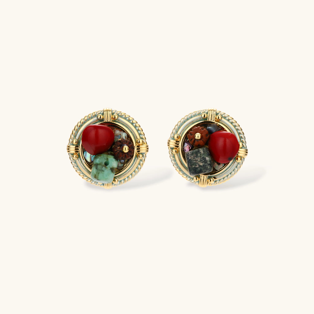 Pair of round gold-plated stud earrings with rope-twist borders, a red bead, brown wood bead and green turquoise on cream.